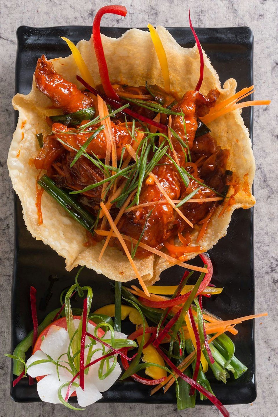 Chicken dish in a crispy bowl garnished with fresh vegetables.