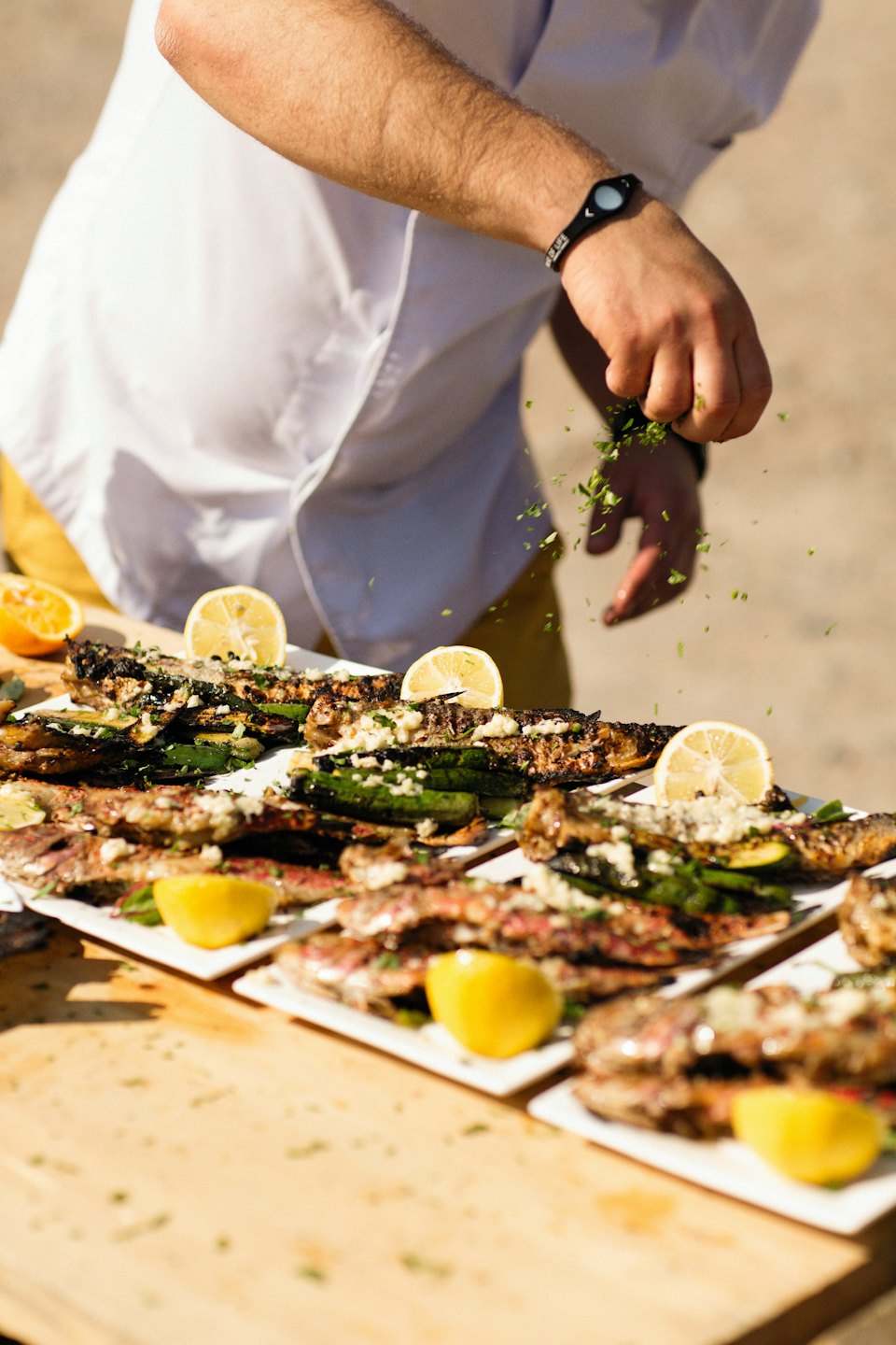 Chef garnishing grilled fish with fresh herbs and lemon.