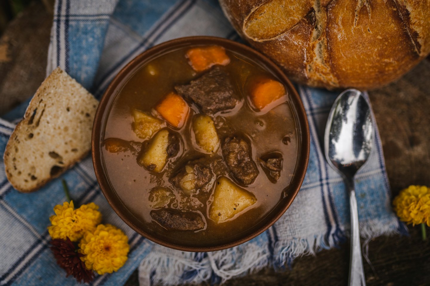 Hearty beef stew in a bowl with bread on a checkered cloth.
