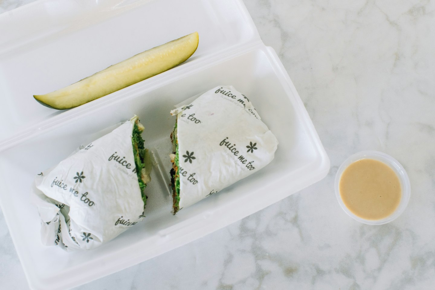 Healthy veggie wrap with pickle and sauce in a compostable container.