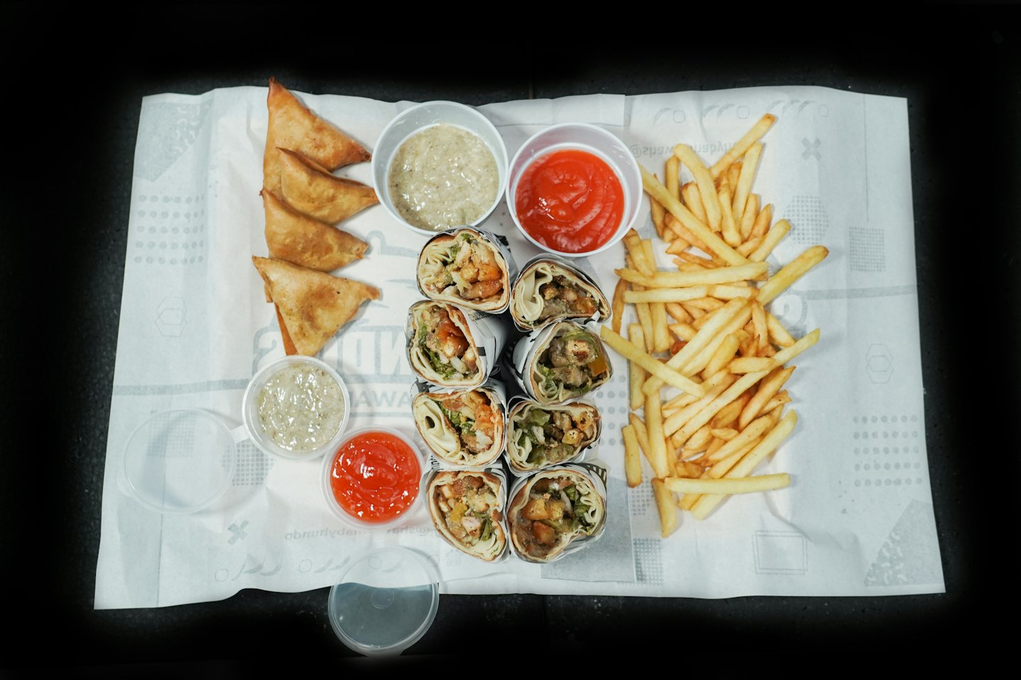 Arrangement of sliced wraps, fries, samosas, and dipping sauces.