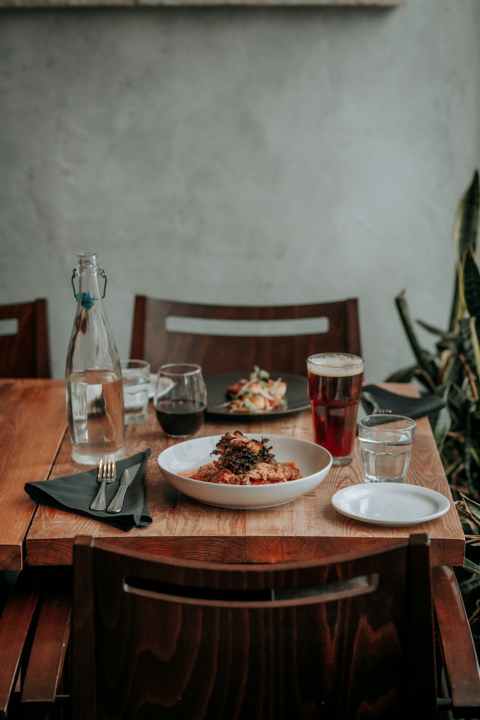 Two place settings on a rustic table with wine and beer.